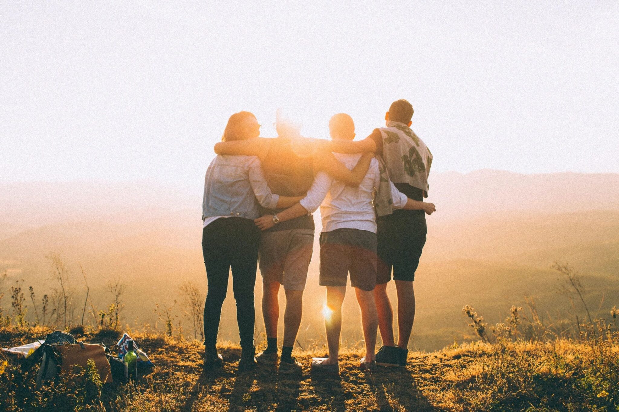 Four friends embracing at sunset on a hilltop.