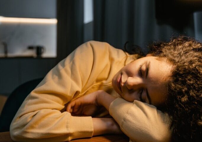 A person resting their head on a desk, appearing tired or contemplative.