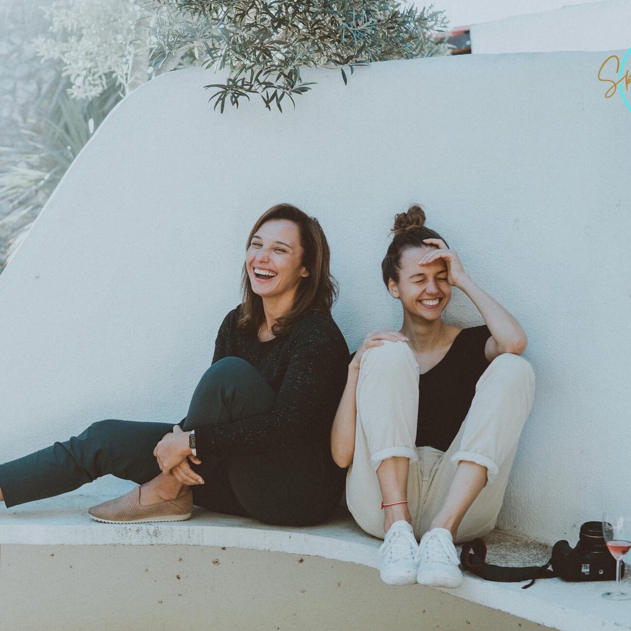 Two young women sitting and smiling outdoors on a white bench.