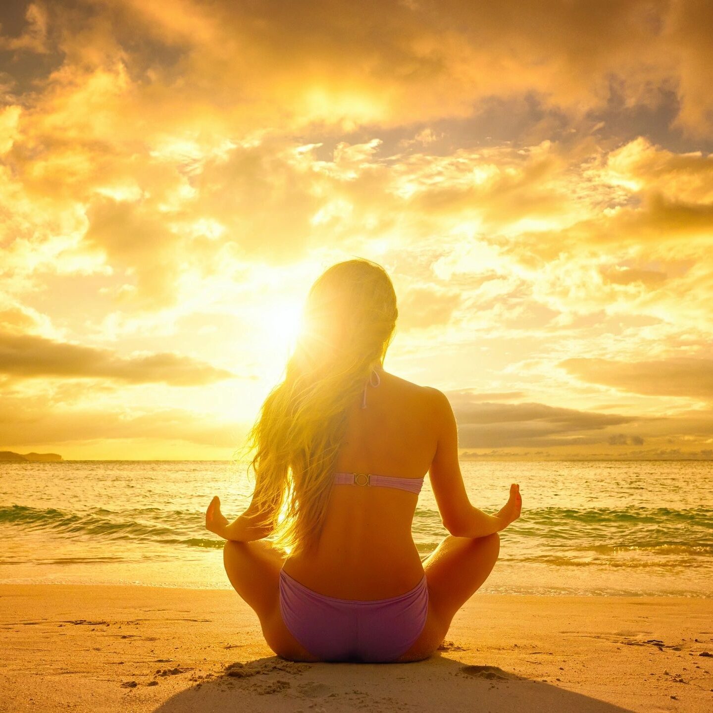 Person meditating on beach during vibrant sunset.