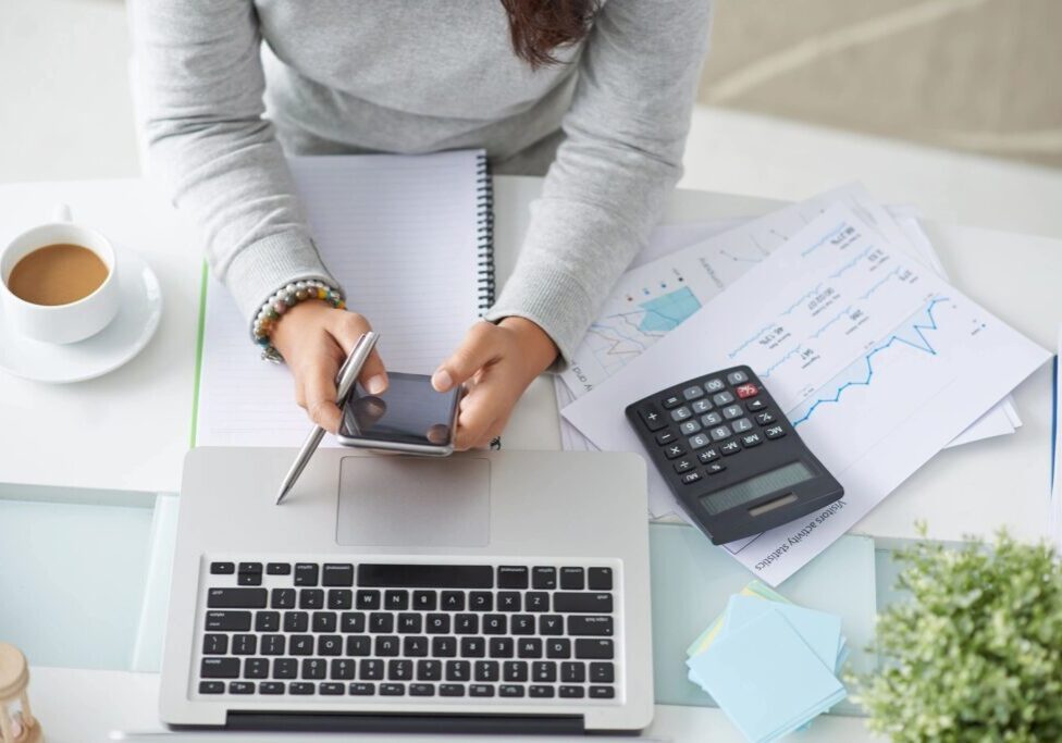 Person using smartphone and laptop with calculator nearby.