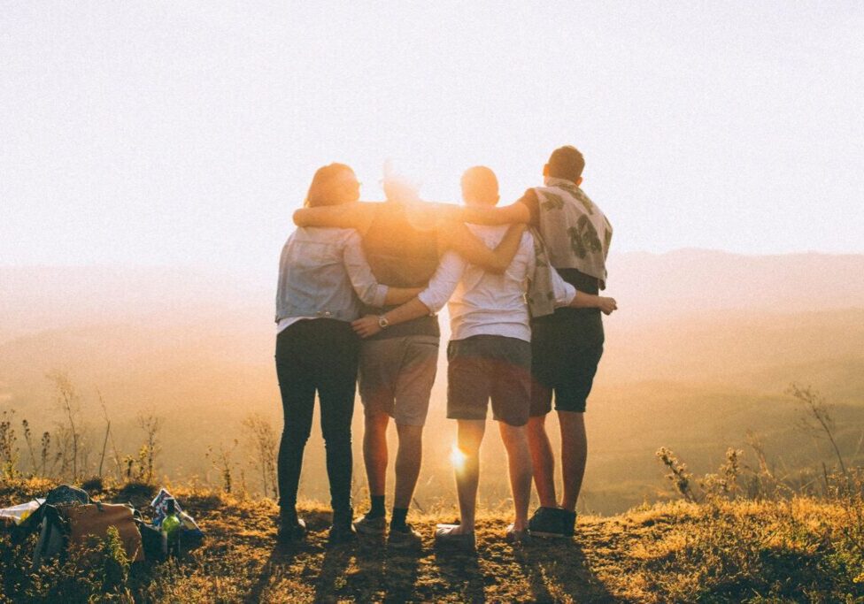 Four friends embracing at sunset on a hilltop.